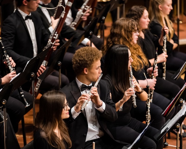 Male student playing a flute with other students playing woodwind instruments around him in a concert