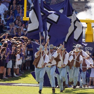 Dressed like cowboys, the TCU Rangers run with large flags at a football game