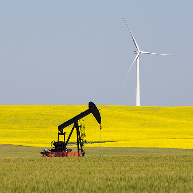 An open field is home to both a pumpjack and a wind turbine