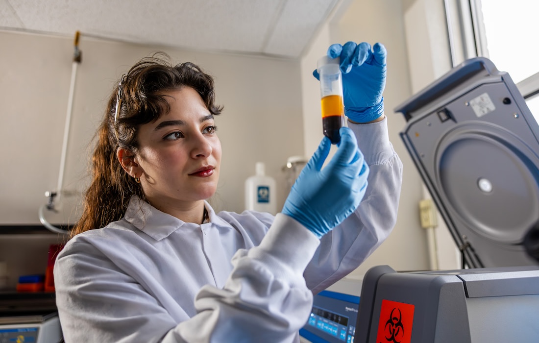 Student in white coat examines vial