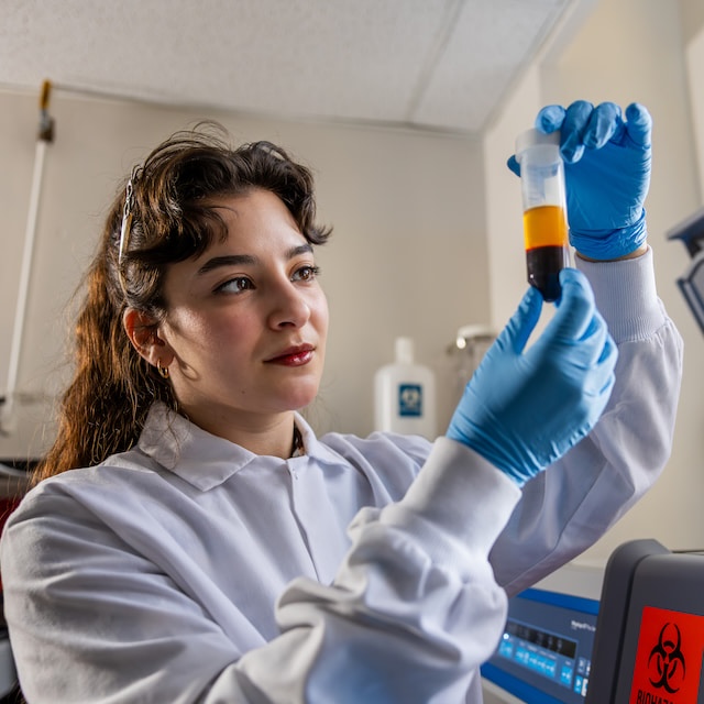 Student in white coat examines vial