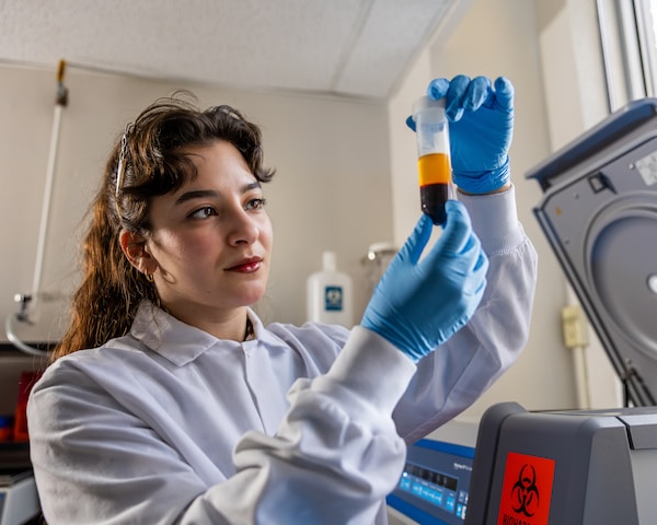 Student in white coat examines vial