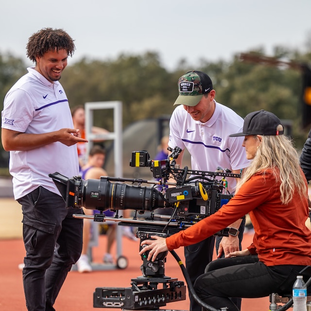 Three people set up a camera on location on the TCU campus
