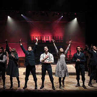 Student actors in a theatrical production of Spring Awakening sing together on stage