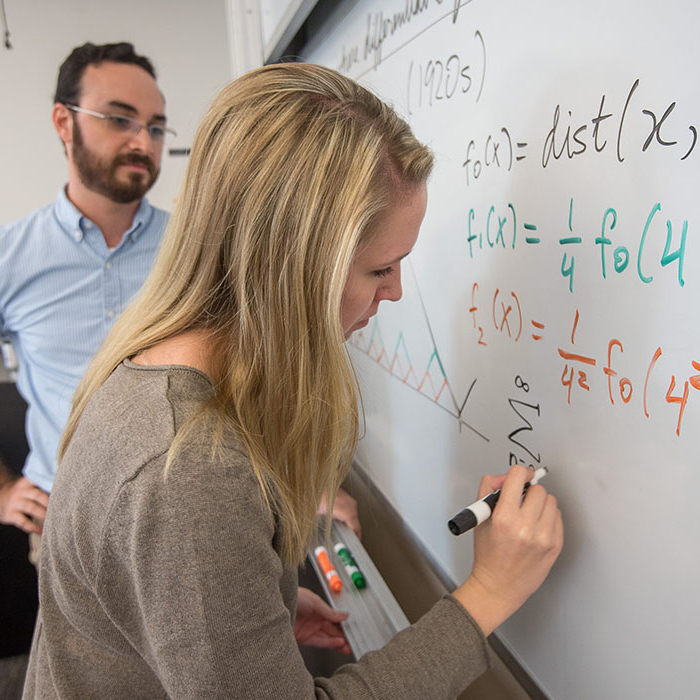 Female student doing math on whiteboard with professor