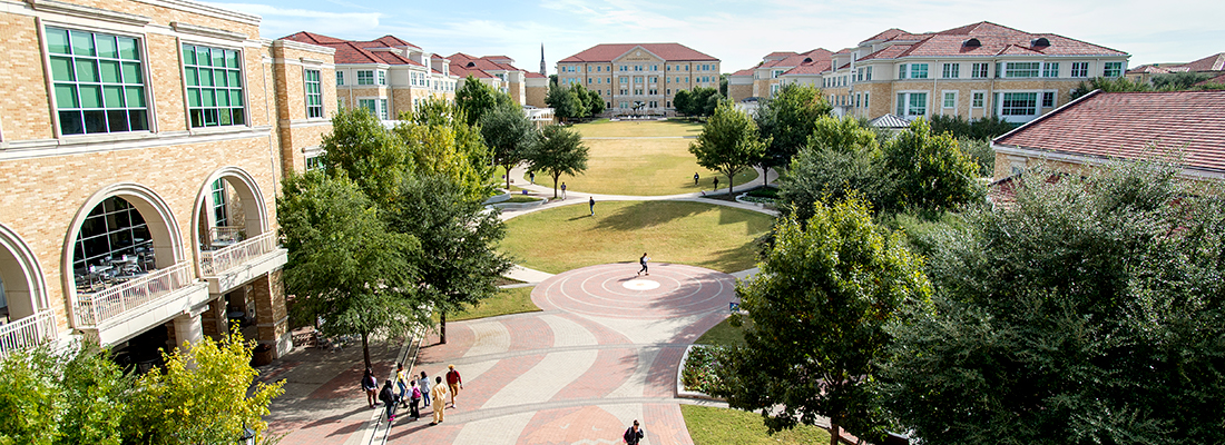 High up view of the TCU campus commons with scattered groups of pedestrians. Frog Fountain is visible in the distance and a huge horned frog logo can be seen on the brick walkway