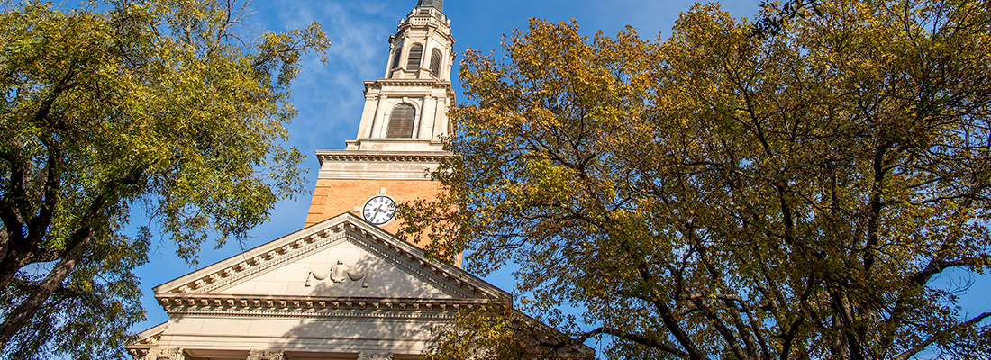 The steeple of the Robert Carr Chapel on the TCU campus, framed by trees and a blue sky.