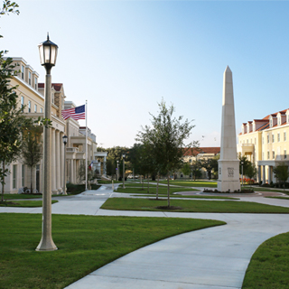 Exterior of the Greek Village at TCU, where a tall obelisk monument bearing greek letters is surrounded group of sorority and fraternity houses 