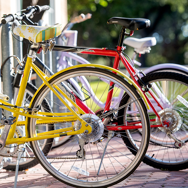 Close up of a bicycle rack on the TCU campus with pink, red, and yellow bikes