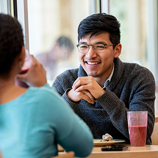 A young male student wearing glasses smiles across a table at a young woman in Market Square, the main TCU dining hall.