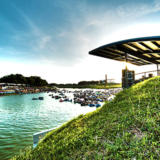 A cluster of people in inflated black inner tubes floats down the Trinity River with a portion of the Fort Worth skyline in the background