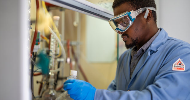 Male student wearing goggles and a lab coat works with samples