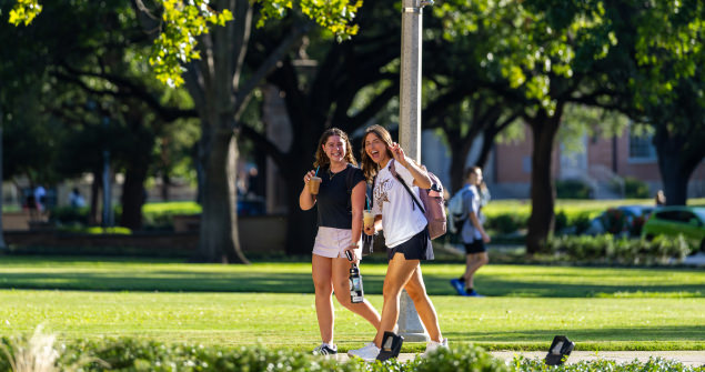 Two female students make the Go Frogs sign as they walk across campus