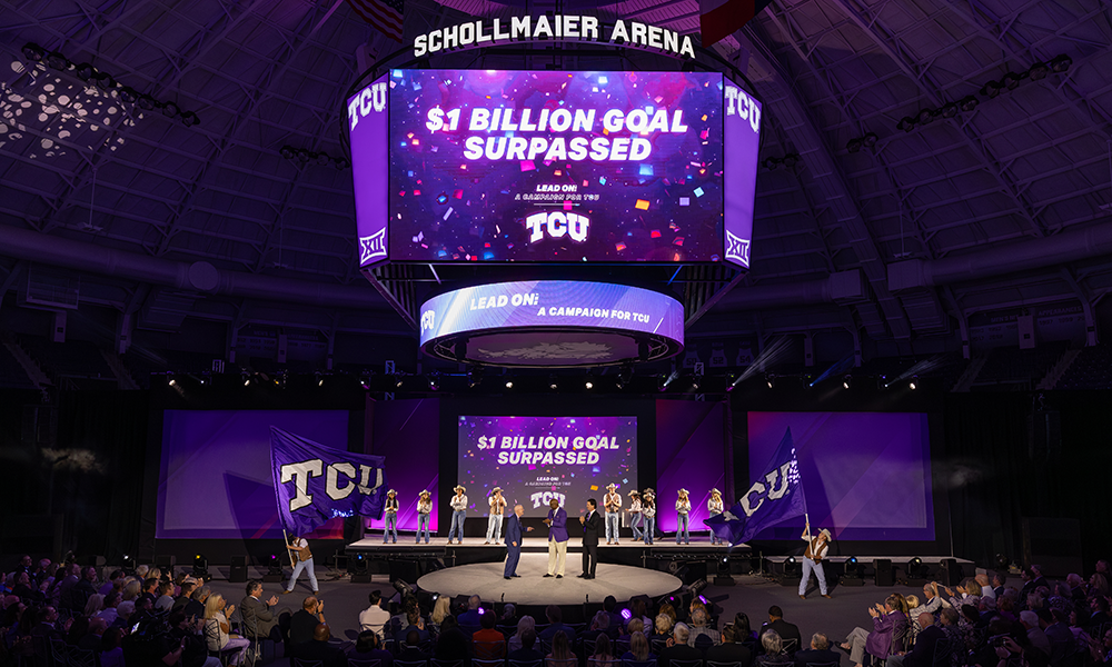 three people on a stage with a jumbotron overhead