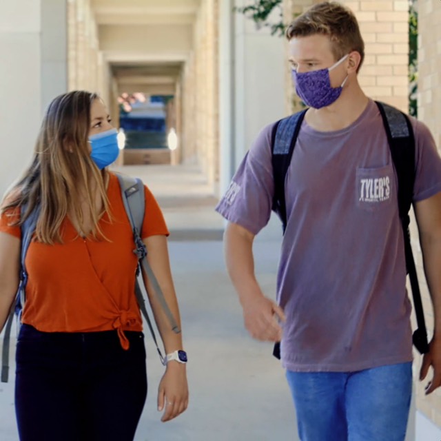 Students walking across campus, each wearing a face covering